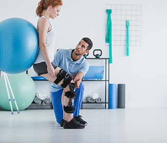 A woman with a knee brace is holding an exercise ball.